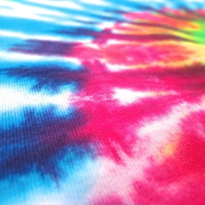 May include: Close-up of a tie-dye fabric with a swirling pattern of blue, pink, white, and yellow colors.