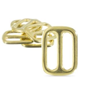 Puede incluir: Un cierre deslizante de metal dorado de cerca. La hebilla tiene dos ranuras paralelas y está diseñada para usarse con correas o cinturones.