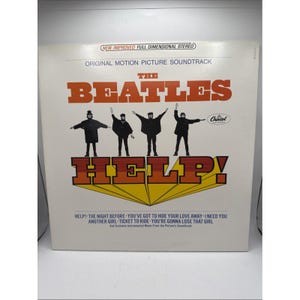 May include: A white vinyl record jacket for The Beatles Help! original motion picture soundtrack. The cover features the band members in black silhouettes, the red title HELP!, and a tracklist including The Night Before and Ticket to Ride.
