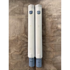 Può includere: Due componenti cilindrici identici in plastica bianca con finitura liscia. Ogni pezzo presenta un piccolo pulsante blu vicino alla parte superiore, due rientranze circolari lungo la lunghezza e una base di connessione blu all'estremità inferiore.