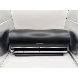 Puede incluir: Una funda de almacenamiento de CD/DVD discgear negra. La funda es cilíndrica con ribetes plateados y blancos. El logotipo de discgear es visible. La funda está abierta, revelando el área de almacenamiento de discos.