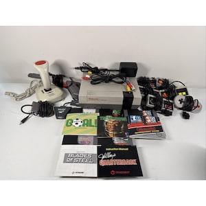 以下が含まれることがあります： コンソール、コントローラー、ゲームカートリッジ、取扱説明書を含む、Nintendo Entertainment System（NES）の完全なセット。コンソールはグレーと黒で、「Blades of Steel」や「Tecmo Bowl」などの複数のコントローラーとゲームカートリッジがあります。