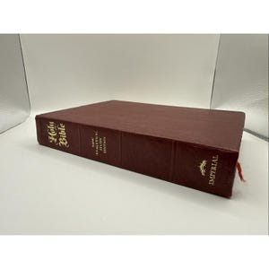 May include: A burgundy-colored Holy Bible with gold lettering. The book is labeled "New Analytical Study Edition" and "Imperial". A red ribbon bookmark is visible.