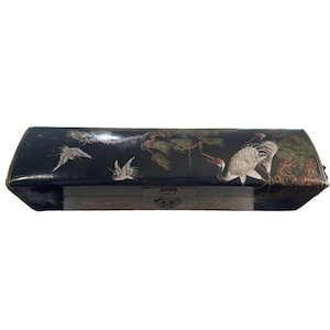 May include: Black lacquered box with a hinged lid and clasp. The box is decorated with painted cranes, pine branches, and foliage in shades of white, red, and green. The box has a rectangular shape with rounded edges.