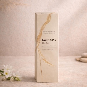 Könnte beinhalten: Eine beige rechteckige Schachtel mit "God's SPA BLISS" Premium-Duftdiffusor-Stäbchen. Die Schachtel hat goldfarbene, blattartige Akzente und Text. Der Text enthält "Jasmin, Geranie, Moschus" und "100 ml / 3,4 fl.oz.".