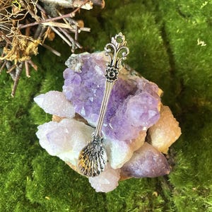 May include: A silver spoon with an ornate design, resting on a bed of purple and white crystals.