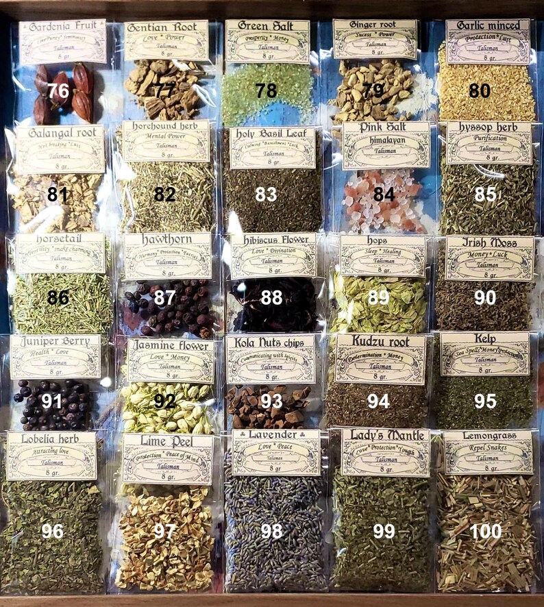 May include: A wooden display case filled with small, clear plastic bags containing various dried herbs and spices. Each bag has a label with the herb's name and weight. The selection includes gardenia fruit, green salt, and lavender.