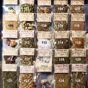 May include: A display cabinet with numerous small bags of dried herbs and spices. Each bag is labelled with the herb's name and weight in grams. Herbs include licorice root, lemon verbena, and marigold. A variety of culinary and medicinal herbs.