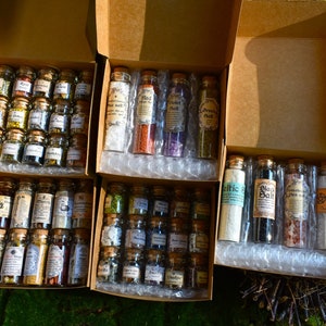 May include: Several cardboard boxes filled with small glass bottles, each containing different herbs and salts. The bottles have cork stoppers and labels. The boxes are arranged on a bed of green moss, with sunlight illuminating the scene.