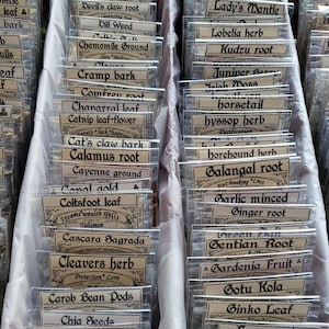 May include: A selection of dried herbs and roots, each in a small, clear plastic bag with a vintage-style label. The image shows various herbs, including Chamomile Ground, Galangal Root, and Angelica Root.