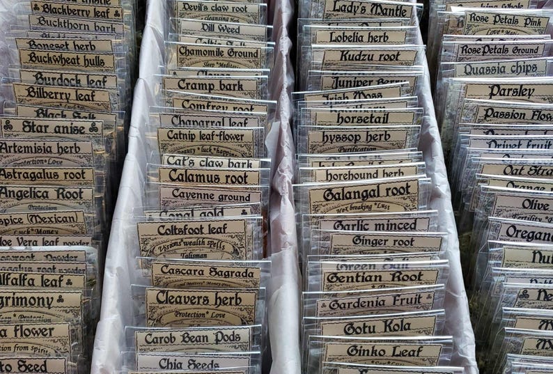 May include: A selection of dried herbs and roots, each in a small, clear plastic bag with a vintage-style label. The image shows various herbs, including Chamomile Ground, Galangal Root, and Angelica Root.