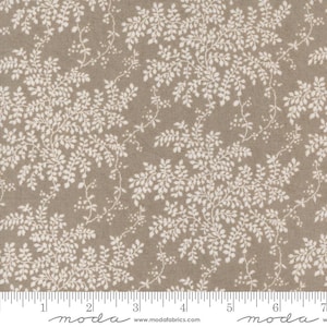 Op de afbeelding: Een beige stof met een wit bloemenpatroon. Het patroon is een herhalend ontwerp van kleine witte bladeren en takken.