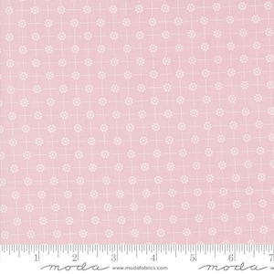 May include: Pink fabric with a white repeating pattern of small flowers on a grid. The fabric is marked with a ruler in inches and the words "moda" and "www.modafabrics.com".