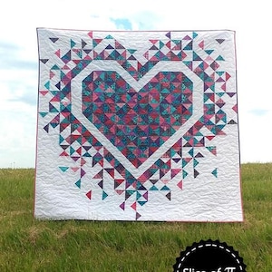 May include: A quilt featuring a large heart design made from colourful fabric triangles. The heart is surrounded by smaller triangles that appear to be exploding outwards. The quilt is displayed on a grassy field with a blue sky in the background. The text "Exploding Heart" is at the top of the image and "Slice of Pi Quilts" is at the bottom.