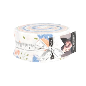 May include: A roll of fabric featuring a floral print in shades of blue, pink, and green. The fabric is wrapped around a measuring tape and tied with a ribbon. The label reads "moda fabrics - supplies".