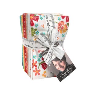 May include: A bundle of patterned fabric squares, tied with a white ribbon printed with a ruler design. The fabric displays floral patterns in red, orange, and turquoise on a white background. A tag with a woman's photo and the "moda FABRICS + SUPPLIES" logo is attached.