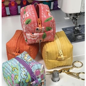 May include: Four small zippered pouches in various colours and patterns, including floral, orange, yellow, and blue. The pouches are labelled "Bitsy Box" and are made by Bodobo Bags by Ticklegrass Designs.