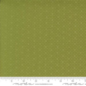 May include: A close-up of green fabric with a repeating pattern of small, off-white dots. The fabric has a textured appearance and is measured with a ruler along the bottom, showing inch increments. The fabric is likely used for quilting or sewing projects.