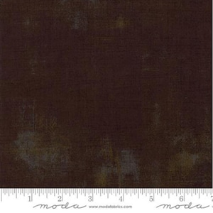 Może przedstawiać: Tkanina w ciemnym brązie o subtelnej, marmurkowej fakturze. Tkanina ma lekko zużyty wygląd z odcieniami złota i szarości. Tkanina jest mierzona w calach za pomocą linijki u dołu obrazu. Linijka ma nadrukowane słowo "moda".