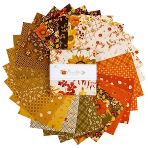 May include: A stack of square fabric swatches arranged in a circular fan pattern. The fabric features autumn-themed prints in shades of orange, yellow, brown, and cream, including sunflowers, pumpkins, and plaid patterns. A white paper band wraps the center.