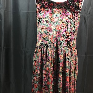 May include: A sleeveless, black velvet dress with a floral print in shades of red, pink, green, and gold. The dress has a scoop neck and a flowy skirt.