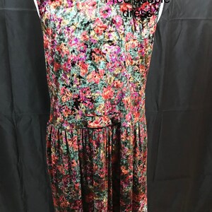 May include: Back view of a sleeveless, floral patterned velvet dress. The dress has a button closure at the waist and a gathered skirt. The text "Free People dress" is visible in the image.