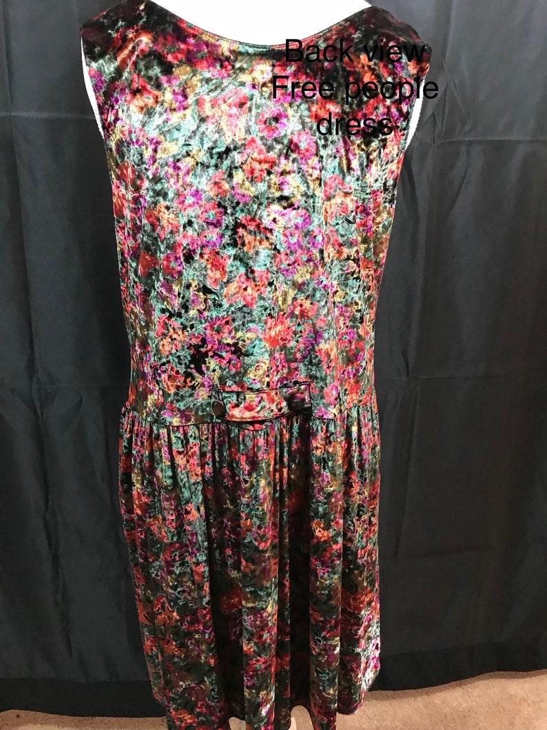 May include: Back view of a sleeveless, floral patterned velvet dress. The dress has a button closure at the waist and a gathered skirt. The text "Free People dress" is visible in the image.