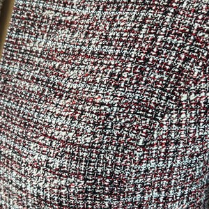 May include: Close-up of a textured fabric with a woven pattern. The fabric features a mix of colours, including red, black, and white, creating a speckled appearance. The weave is tight, suggesting a durable material.