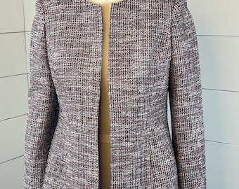 May include: A multi-colored tweed jacket with a collarless design. The jacket features a mix of burgundy, white, and gray threads woven together. It has long sleeves and a tailored fit, displayed on a mannequin.
