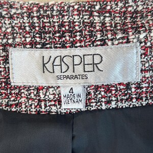 May include: Close-up of a tweed jacket with a black lining. The jacket is a mix of red, black, and white threads. The label reads "KASPER SEPARATES" and "4 MADE IN VIETNAM".