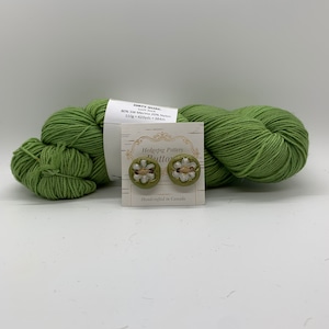 May include: A skein of green yarn with a label that reads "Dirty Quac 80% SW Merino 20% Nylon 110g 420yds 384m" and a card with two green and white floral buttons that reads "Hedgepig Pottery Button Handcrafted in Canada".