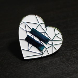 May include: A white enamel heart-shaped pin with a geometric design and two dark blue stripes in the center.