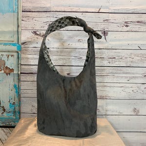 May include: A gray and black fabric tote bag with a checkered pattern on the inside. The bag has a single strap and is made of a soft, textured material.