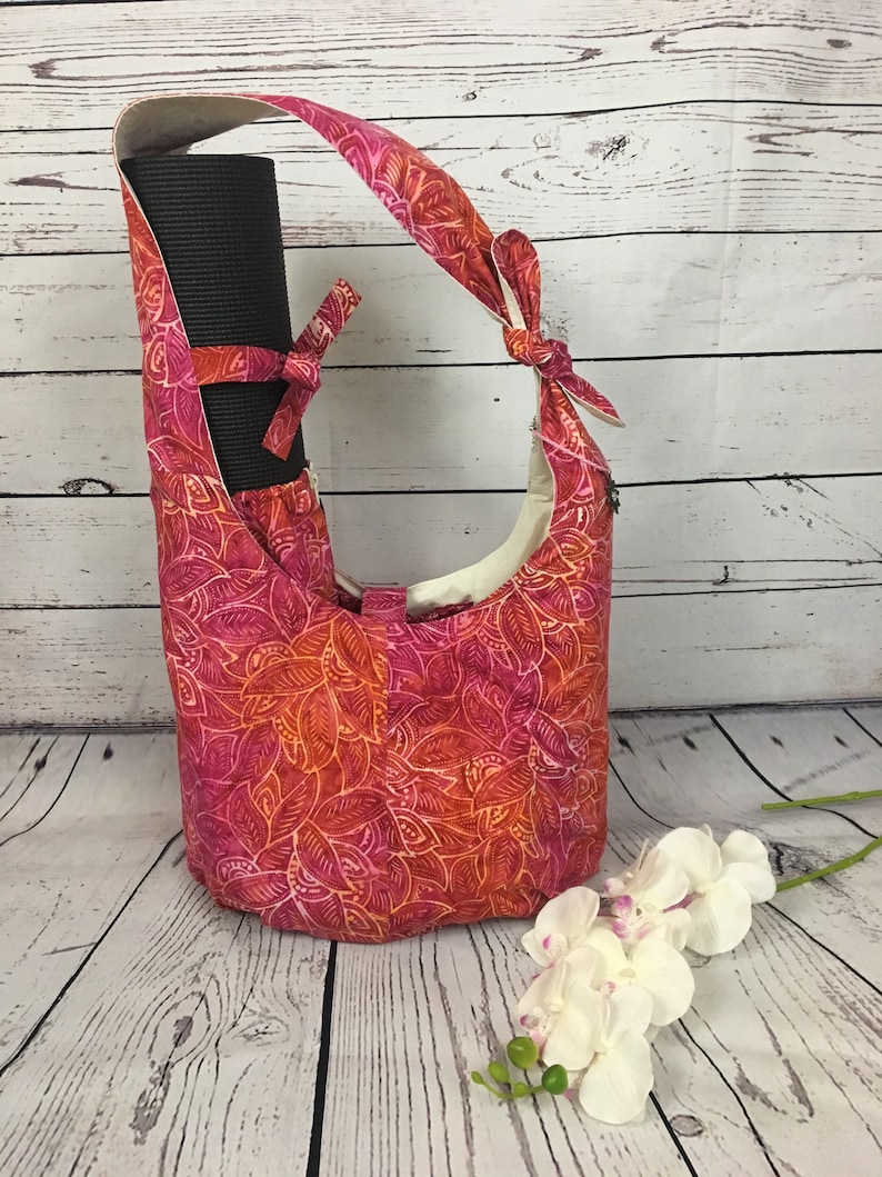 May include: A pink and orange floral yoga mat bag with a black yoga mat inside. The bag has a long strap and a knotted handle.