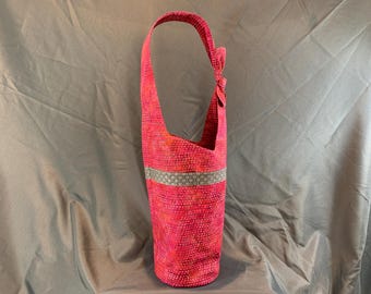 May include: A tall, pink fabric bag with a single shoulder strap. The bag has a textured pattern and a decorative band of gray and white fabric. The strap is knotted at the top. The bag is approximately 20 inches tall.