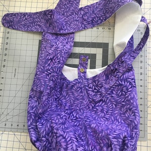 May include: A purple tote bag with a white leaf pattern. The bag has a white lining and a single snap closure.