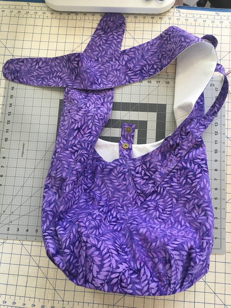 May include: A purple tote bag with a white leaf pattern. The bag has a white lining and a single snap closure.