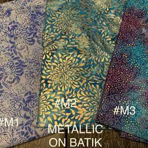 May include: Three fabric swatches with metallic gold accents on a blue and purple batik background. The swatches are labeled #M1, #M2, and #M3. The text "Metallic on Batik" is printed below the swatches.