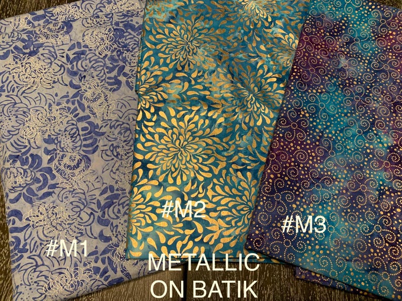 May include: Three fabric swatches with metallic gold accents on a blue and purple batik background. The swatches are labeled #M1, #M2, and #M3. The text "Metallic on Batik" is printed below the swatches.