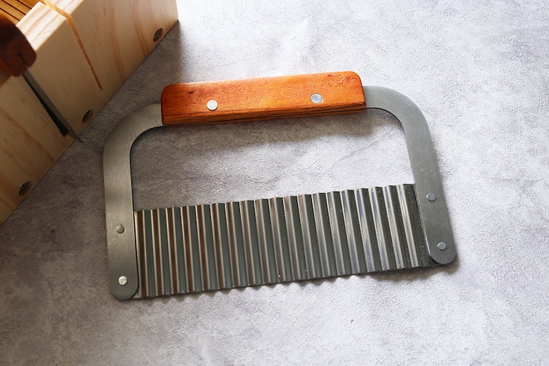 Puede incluir: Un cuchillo de acero inoxidable con borde ondulado y mango de madera. El cuchillo est&aacute; dise&ntilde;ado para cortar verduras en formas decorativas.