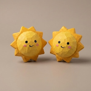May include: Two yellow sun-shaped wooden carvings with faceted surfaces. Each sun features a hand-painted face with two black circular eyes, a simple curved black mouth, and two small pink circular cheeks. The suns have pointed rays.