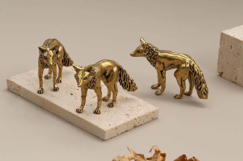 Op de afbeelding: Drie messing vossenbeeldjes. Twee staan op een rechthoekige steen en &eacute;&eacute;n staat apart. De vossen hebben gedetailleerde vacht en staan in verschillende poses. De achtergrond is neutraal van kleur.