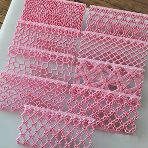 Op de afbeelding: Set van acht roze plastic taartdecoratiegereedschappen met verschillende reliëfpatronen. De gereedschappen zijn ontworpen om decoratieve randen op taarten en gebak te creëren.