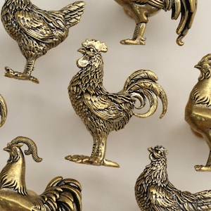 May include: Several brass-toned rooster figurines. The roosters are depicted in different stances, with intricate feather detailing and prominent combs. These figurines are likely decorative pieces, possibly for home decor or as collectibles.