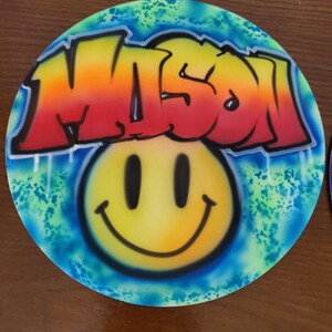 Puede incluir: Un fondo redondo azul y verde con una cara sonriente amarilla y la palabra "MISO" en colores arcoíris en estilo graffiti.