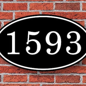 May include: Black oval-shaped house number sign with white numbers "1593" against a brick wall background.