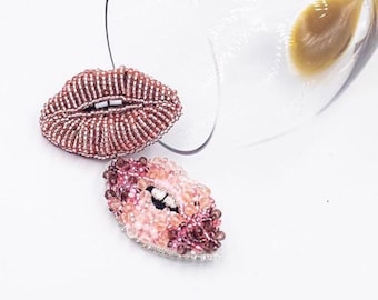 May include: Two beaded lips brooches, one in pink and one in a darker shade of pink. The brooches are made of small beads and are shaped like lips.