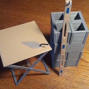 May include: A miniature construction set with a gray concrete block, a wooden level, and a small trowel on a folding table.