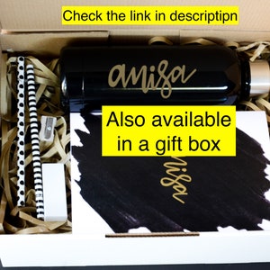 May include: A white gift box filled with brown packing paper and a black water bottle with the name "anisa" written in gold lettering. The box also contains a black and white notebook with the same name written in gold lettering. The text "Also available in a gift box" is written in yellow on a black background.