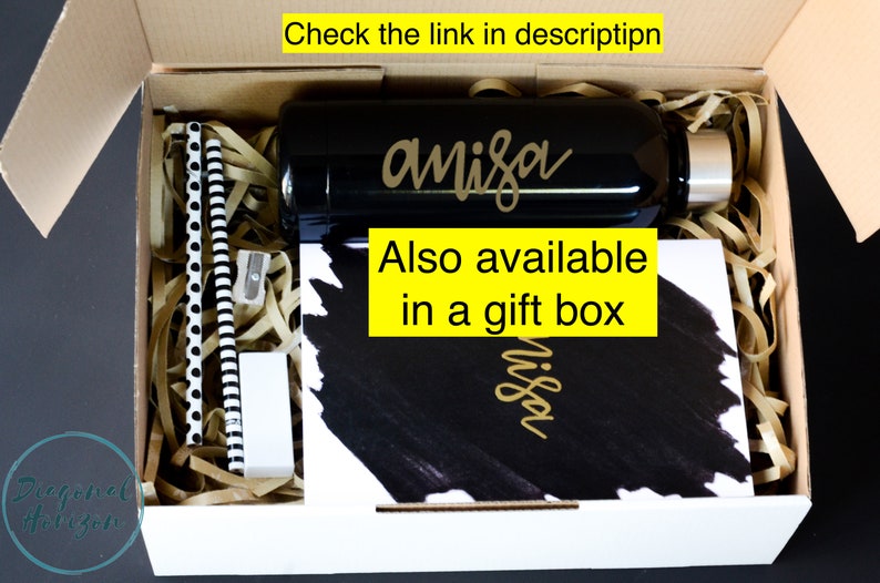 May include: A white gift box filled with brown packing paper and a black water bottle with the name "anisa" written in gold lettering. The box also contains a black and white notebook with the same name written in gold lettering. The text "Also available in a gift box" is written in yellow on a black background.